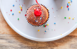 Vanilla cupcake with chocolate frosting, sprinkles and a cherry on top.
